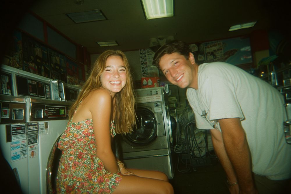 A couple smiling side by side in a laundromat.